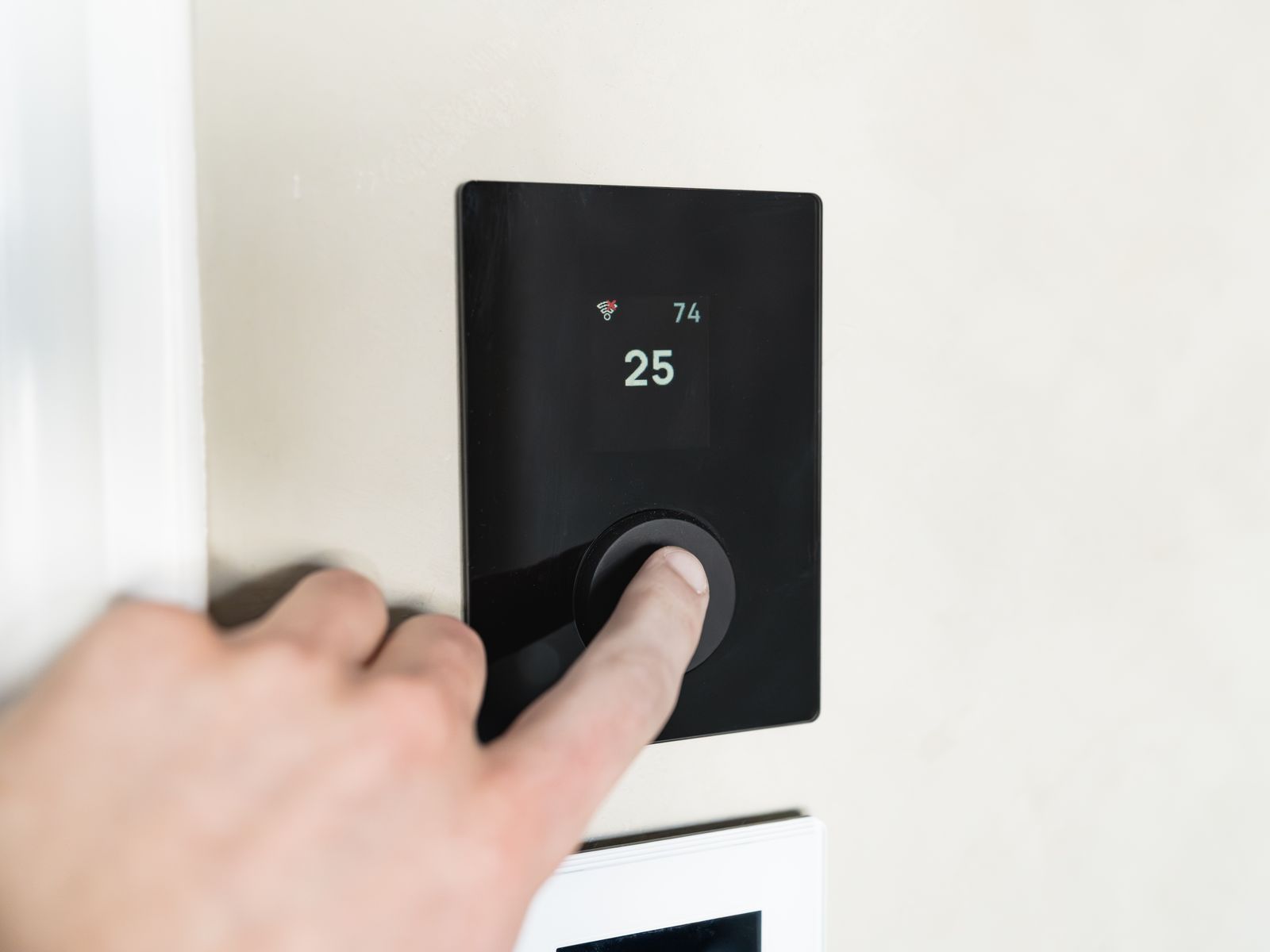 Main réglant un thermostat connecté fixé au mur