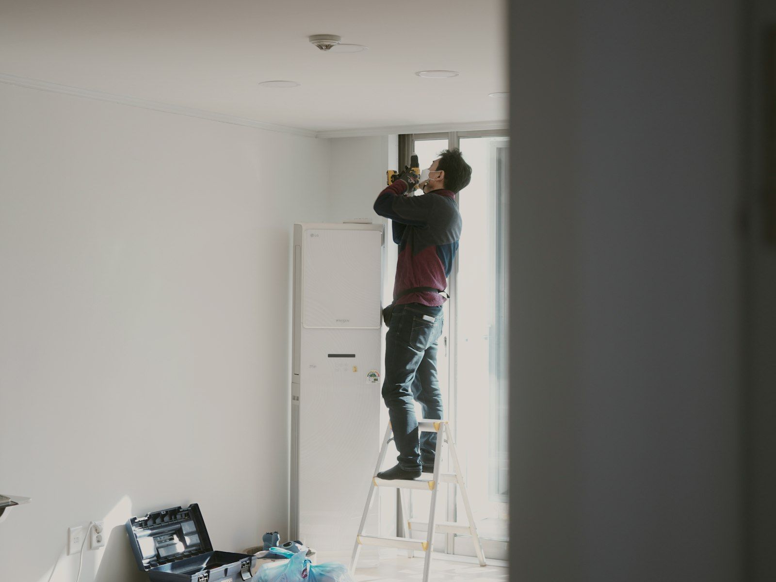 Électricien sur un escabeau dans une pièce neuve aux murs blancs