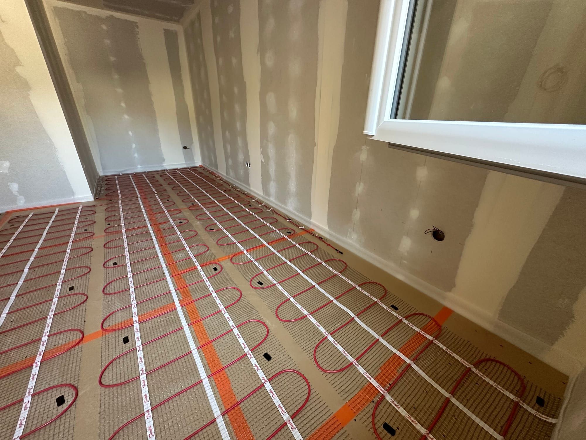 Trame de plancher chauffant électrique agrafée sur une dalle, dans une pièce aux murs en plâtre