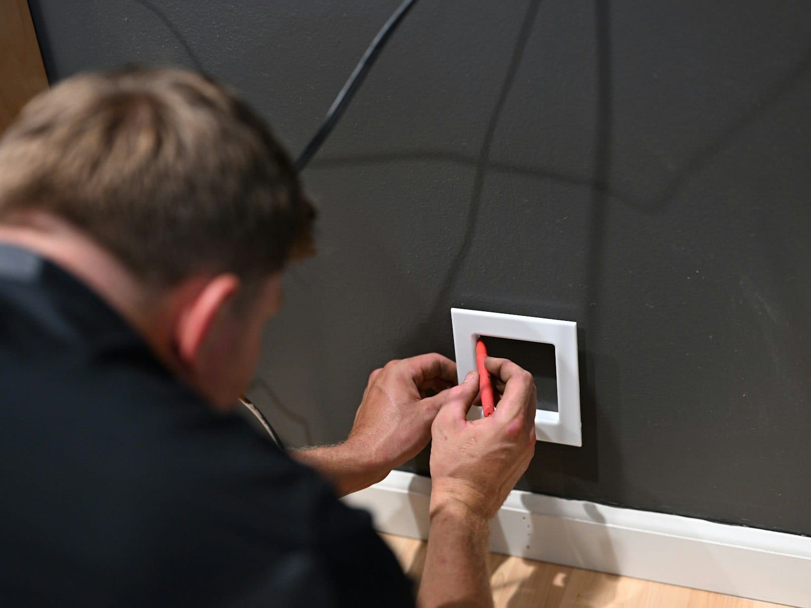 Électricien fixant un appareillage mural sur une cloison sombre