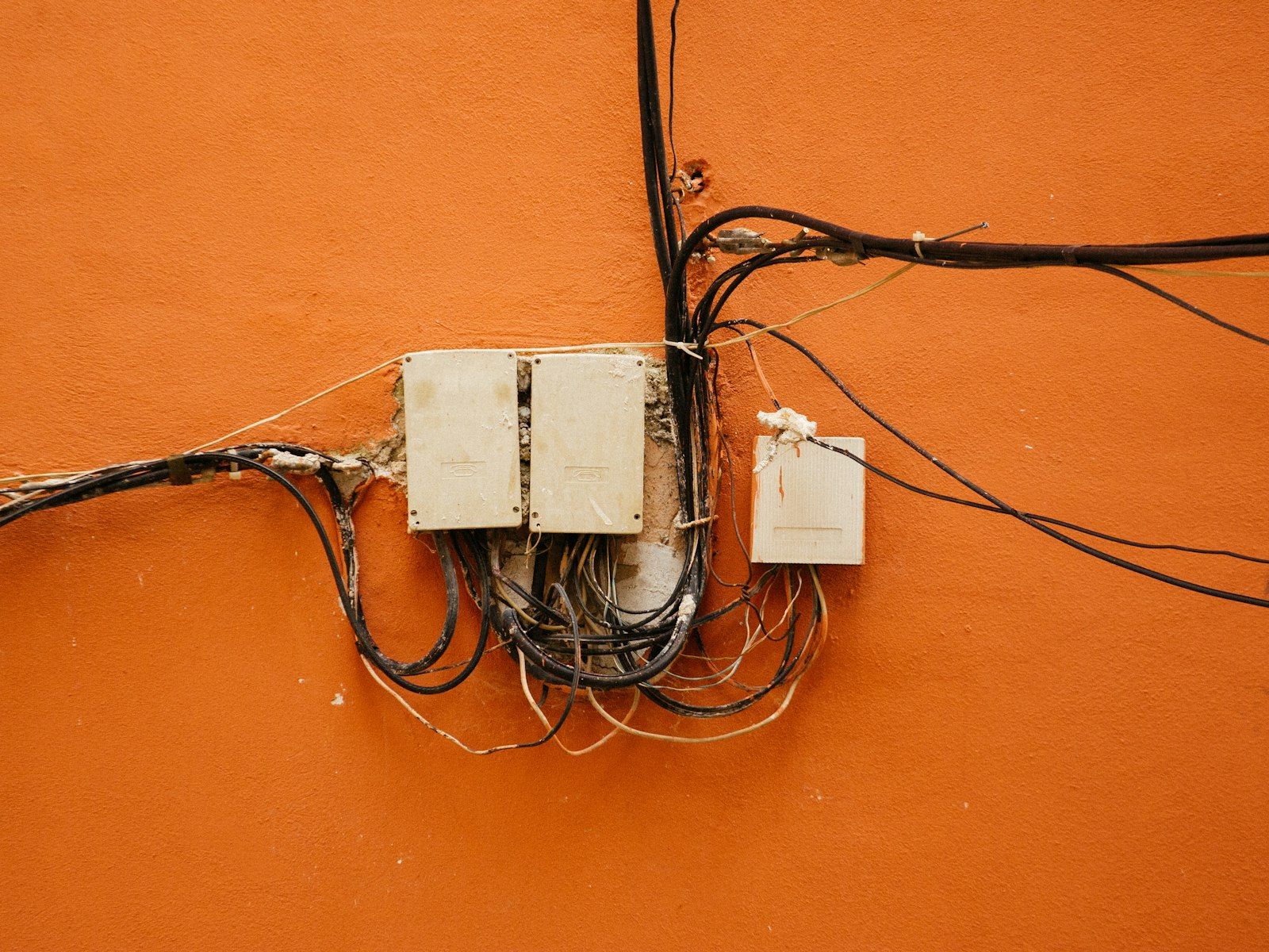 Ancien câblage apparent et boîtiers sur un mur orange